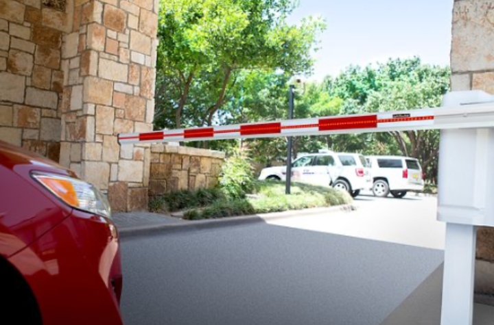 LiftMaster barrier arm gate access system in action, with a car waiting for the gate to open, and a residential community in the background.