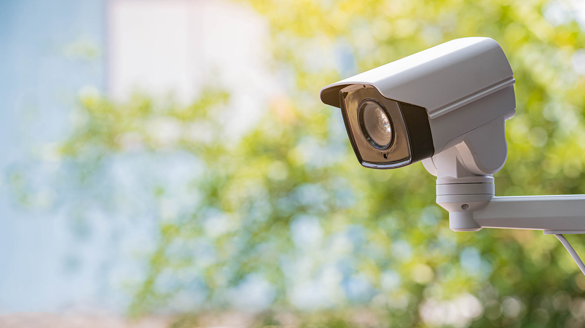 An IP bullet type security camera, one of the various types of security cameras, mounted outdoors against a lush green background, showcasing its suitability for outdoor surveillance.
