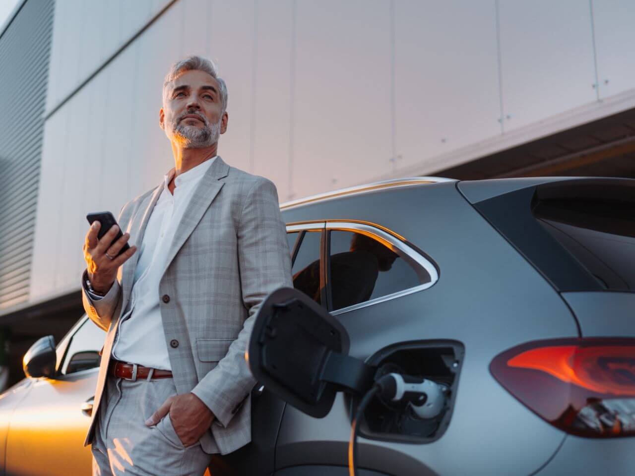 Middle-aged businessman leaning on his charging electric vehicle, representing EV charging for businesses.
